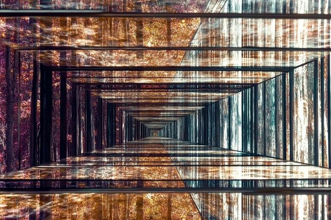 An infinite hallway of mirrors reflects recursively, glowing with soft purple and pink hues against a backdrop of rust and cracked glass.
